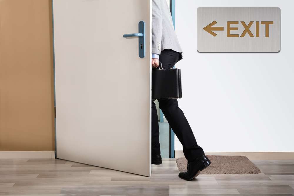 Businessperson,Walking,Out,With,Exit,Sign,On,Wall