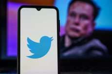 Logo de Twitter en un teléfono con Elon Musk de fondo